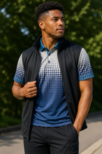 Load image into Gallery viewer, A man wearing a sleeveless black zip-up vest over a blue and white gradient polo shirt, standing outdoors on a paved path with green trees in the background.