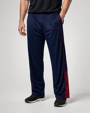 Load image into Gallery viewer, A person wearing navy athletic track pants with red side stripes and red lower-leg panels, paired with black sneakers, photographed against a light gray studio background.