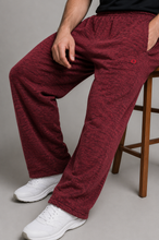 Load image into Gallery viewer, A person seated on a wooden stool wearing heathered burgundy lounge pants with side pockets and white sneakers against a plain gray studio background.