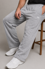 Load image into Gallery viewer, A person wearing heather gray sweatpants with white sneakers, seated on a wooden stool against a plain light gray studio background.