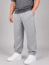 Load image into Gallery viewer, A person wearing heather gray jogger sweatpants with elastic cuffs, paired with a dark gray t-shirt and white sneakers, shown from the waist down against a light gray studio background.