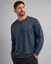Load image into Gallery viewer, A man wearing a heathered navy blue long-sleeve quarter-zip pullover with a small embroidered logo on the left chest, paired with dark pants, against a solid gray studio background.