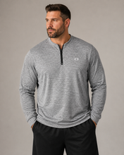 Load image into Gallery viewer, A man wearing a heather gray long-sleeve quarter-zip pullover with a small white logo on the left chest, paired with black pants, against a solid gray studio background.