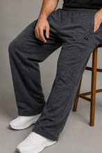 Load image into Gallery viewer, A person wearing dark heather gray lounge pants with white sneakers, seated on a wooden stool against a gray studio background.