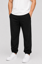 Load image into Gallery viewer, A person wearing black jogger sweatpants with a white t-shirt and white sneakers, shown from the chest down against a light gray studio background.
