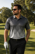 Load image into Gallery viewer, A man wearing a dark gray and white patterned short-sleeve polo shirt, black pants, and sunglasses, standing on a golf course with trees in the background.
