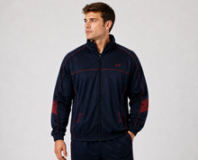 Load image into Gallery viewer, A man wearing a navy blue athletic zip-up jacket with red contrast stitching and red sleeve panels, standing against a light gray studio background.
