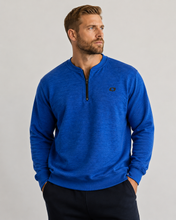 Load image into Gallery viewer, A man wearing a bright blue heathered quarter-zip pullover sweater with a small black logo on the left chest, paired with dark pants, against a plain light gray studio background.
