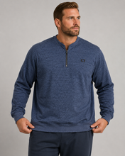 Load image into Gallery viewer, A man wearing a heathered blue long-sleeve quarter-zip pullover sweater with a small embroidered logo on the left chest, paired with dark pants, against a solid gray studio background.
