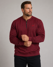 Load image into Gallery viewer, A man wearing a heathered burgundy quarter-zip long-sleeve pullover with a small red embroidered logo on the left chest, paired with black pants, photographed against a neutral gray studio background.
