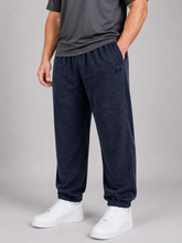 Load image into Gallery viewer, A person wearing dark navy heather jogger sweatpants with an elastic waistband and cuffs, paired with a dark gray t-shirt and white sneakers, shown from the waist down on a light gray studio background.
