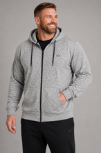 Load image into Gallery viewer, A smiling man wearing a heather gray zip-up hoodie with black drawstrings and a black t-shirt underneath, paired with black sweatpants, against a solid gray studio background.
