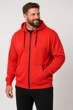 Load image into Gallery viewer, A smiling man wearing a bright red zip-up hoodie with black drawstrings and black pants, photographed against a light gray studio background.

